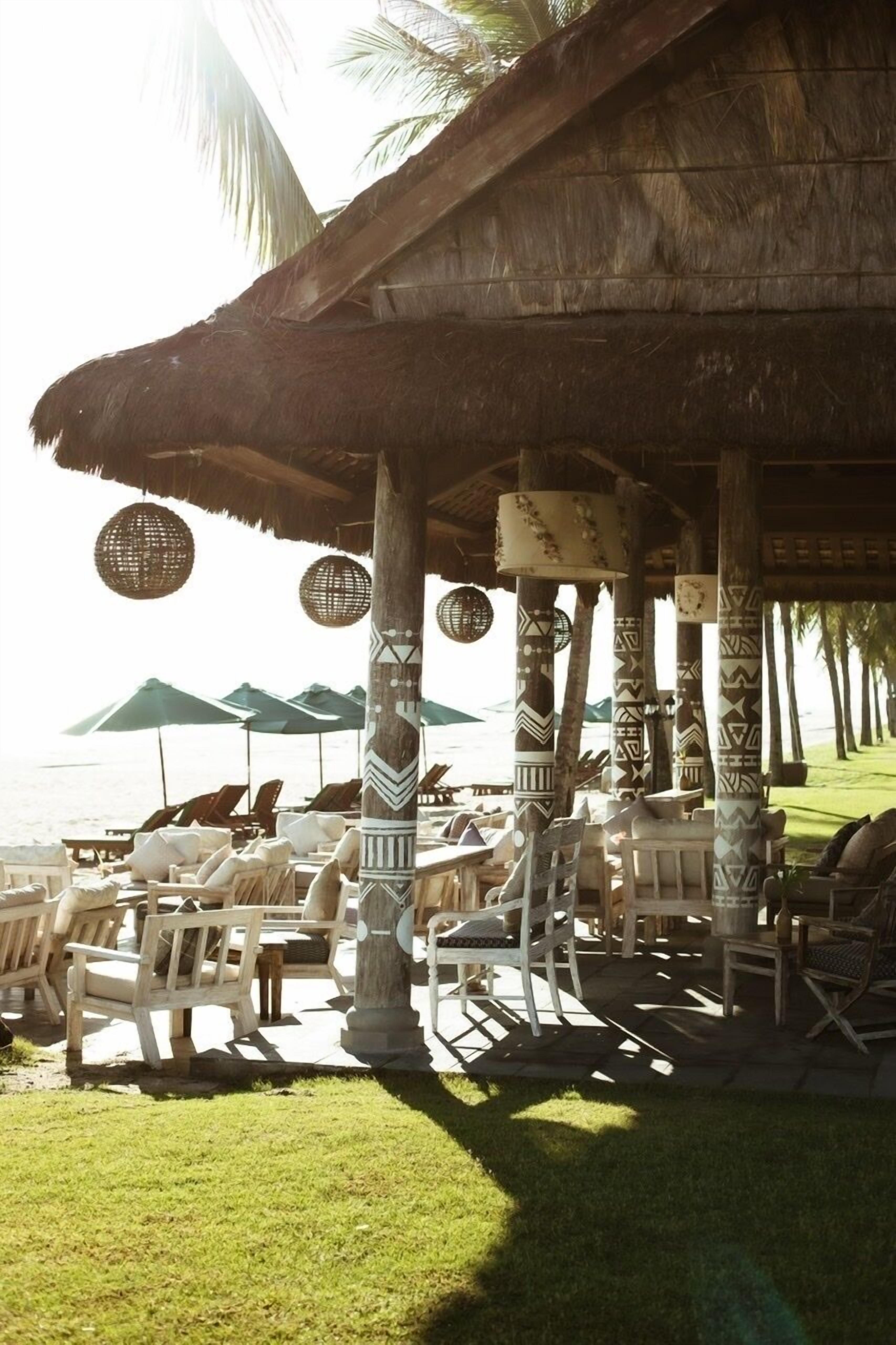 A beachside lounge with thatched roof, patterned pillars, and lounge chairs.