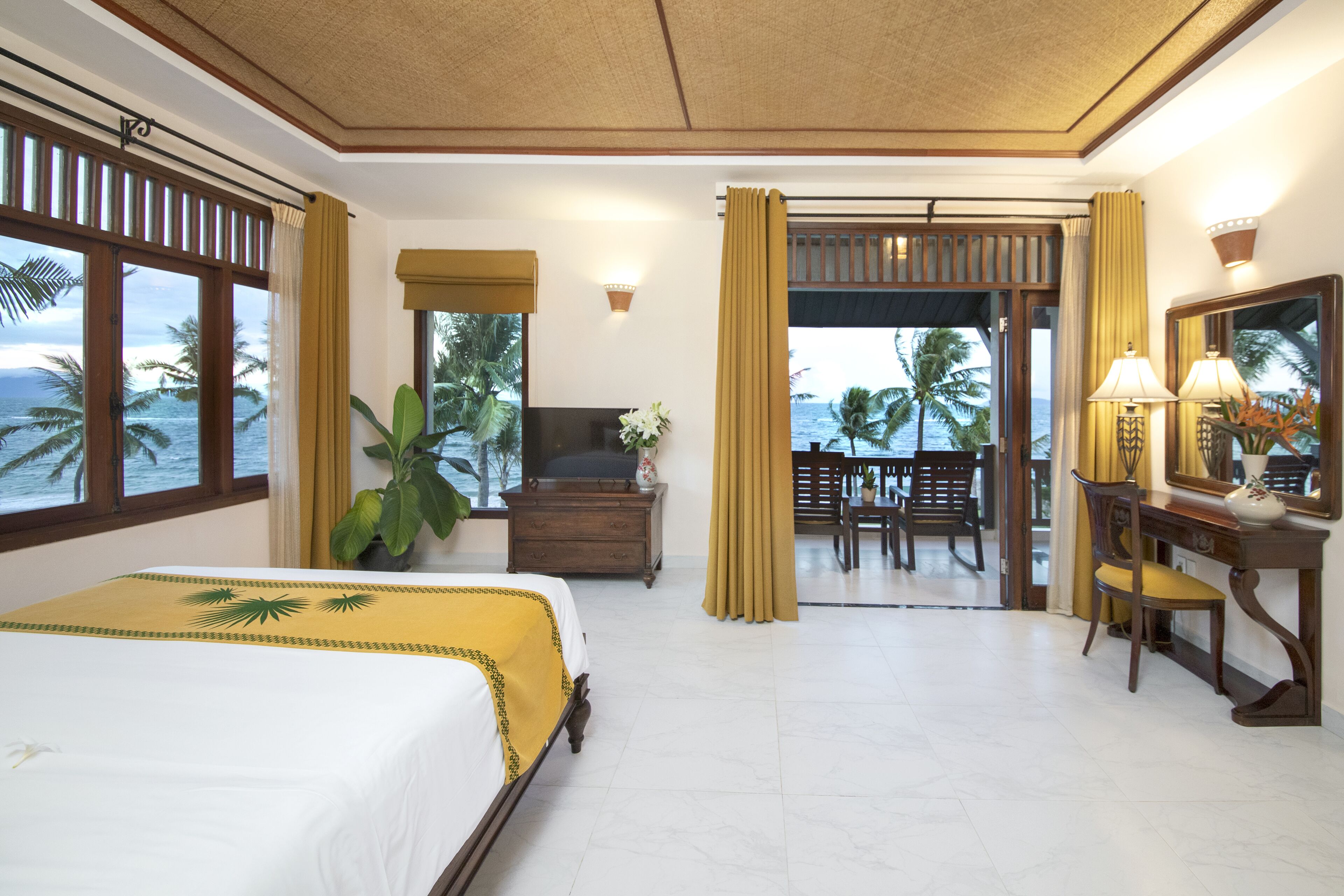 A hotel room with a bed, a desk, a chair, a TV, and a view of the ocean.