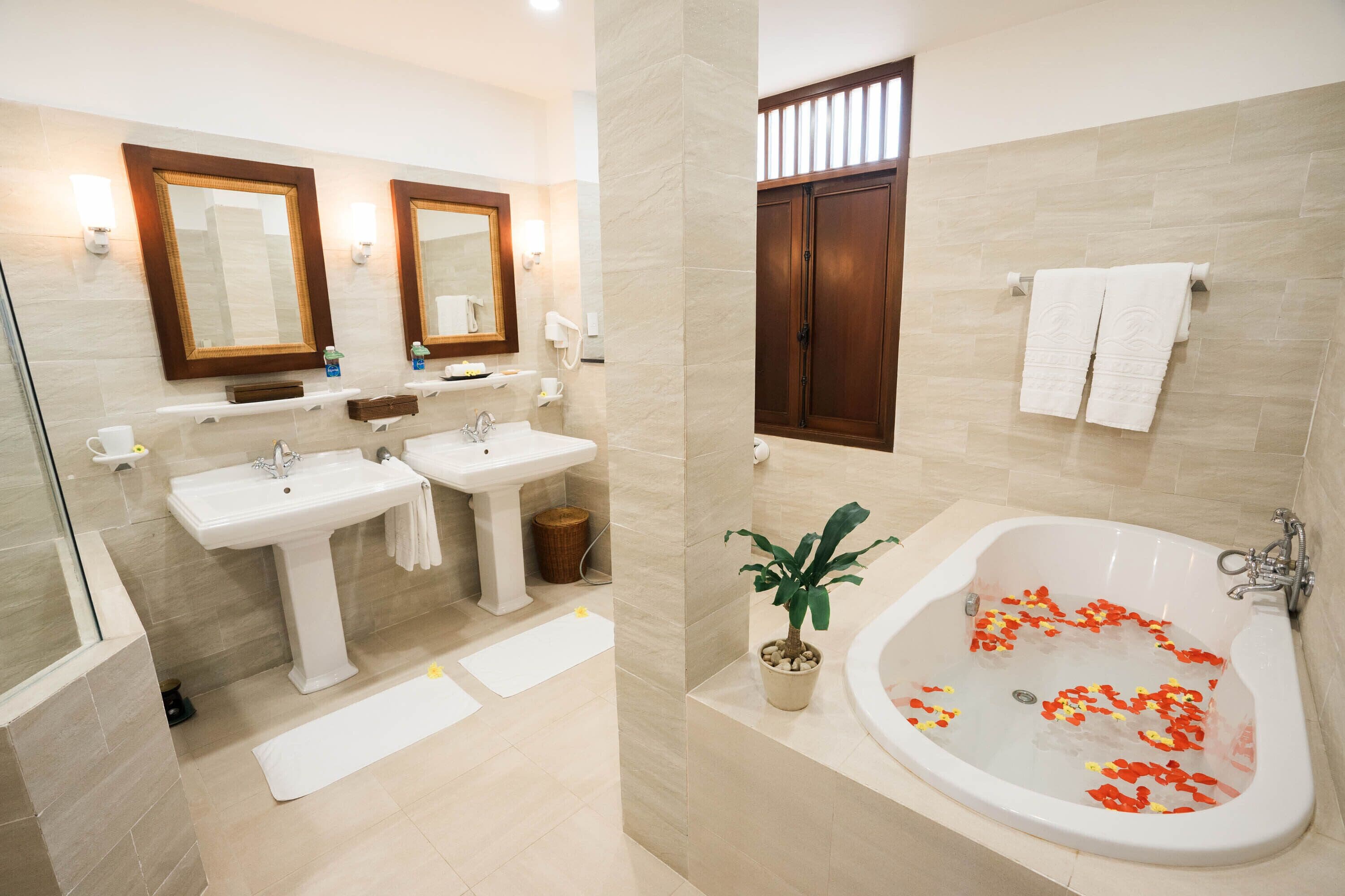 A modern bathroom with two sinks, a bathtub with rose petals, and a potted plant.