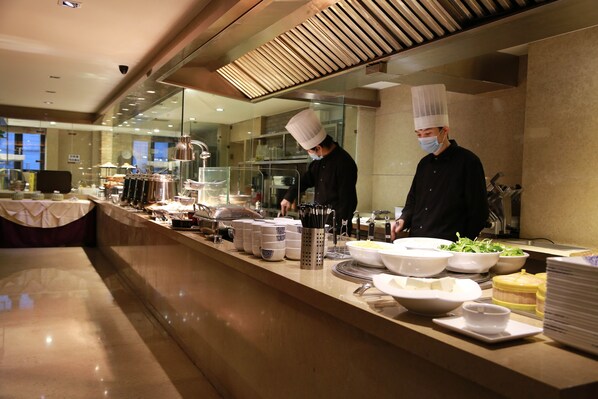 Montaje de bufé con múltiples estaciones de servicio, un chef con uniforme y diversos recipientes de comida.
