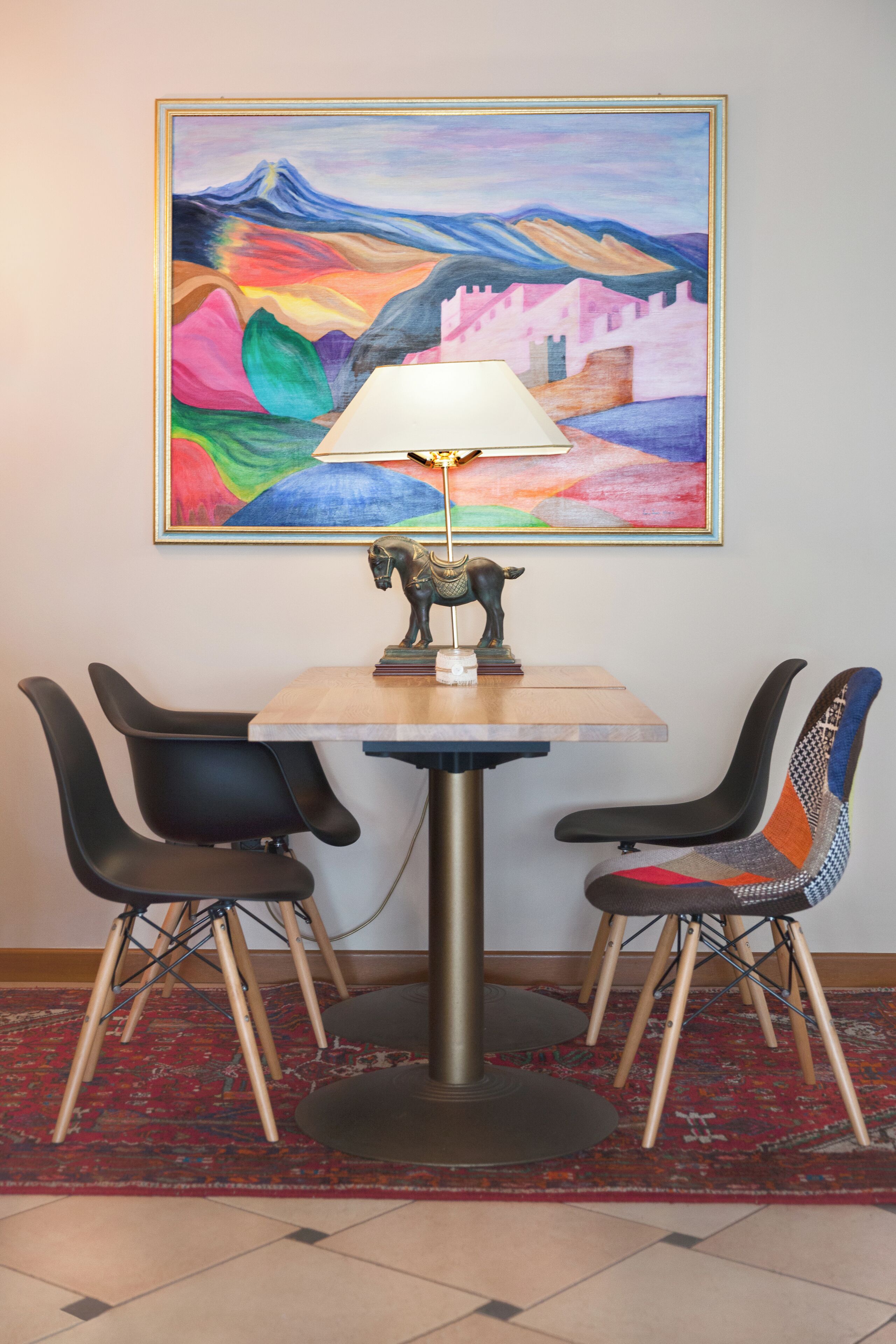 A dining area with a table, chairs, a lamp, and a painting on the wall.