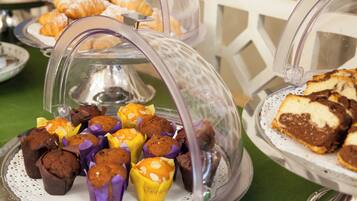 A buffet with various baked goods, including muffins and pastries, displayed on clear glass stands.