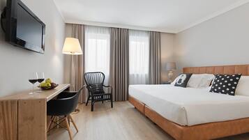A hotel room with a bed, desk, chair, and a television on the wall.