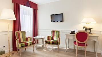Ein Hotelzimmer mit zwei gestreiften Sesseln, einem kleinen runden Tisch, einem Schreibtisch mit Lampe und einem wandmontierten Fernseher.