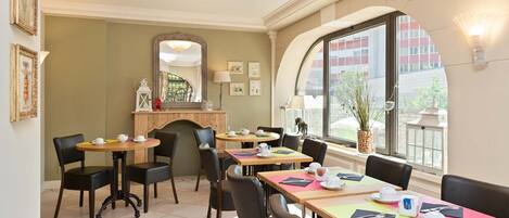 Comedor con varias mesas y sillas, chimenea y un amplio ventanal con vistas al exterior.