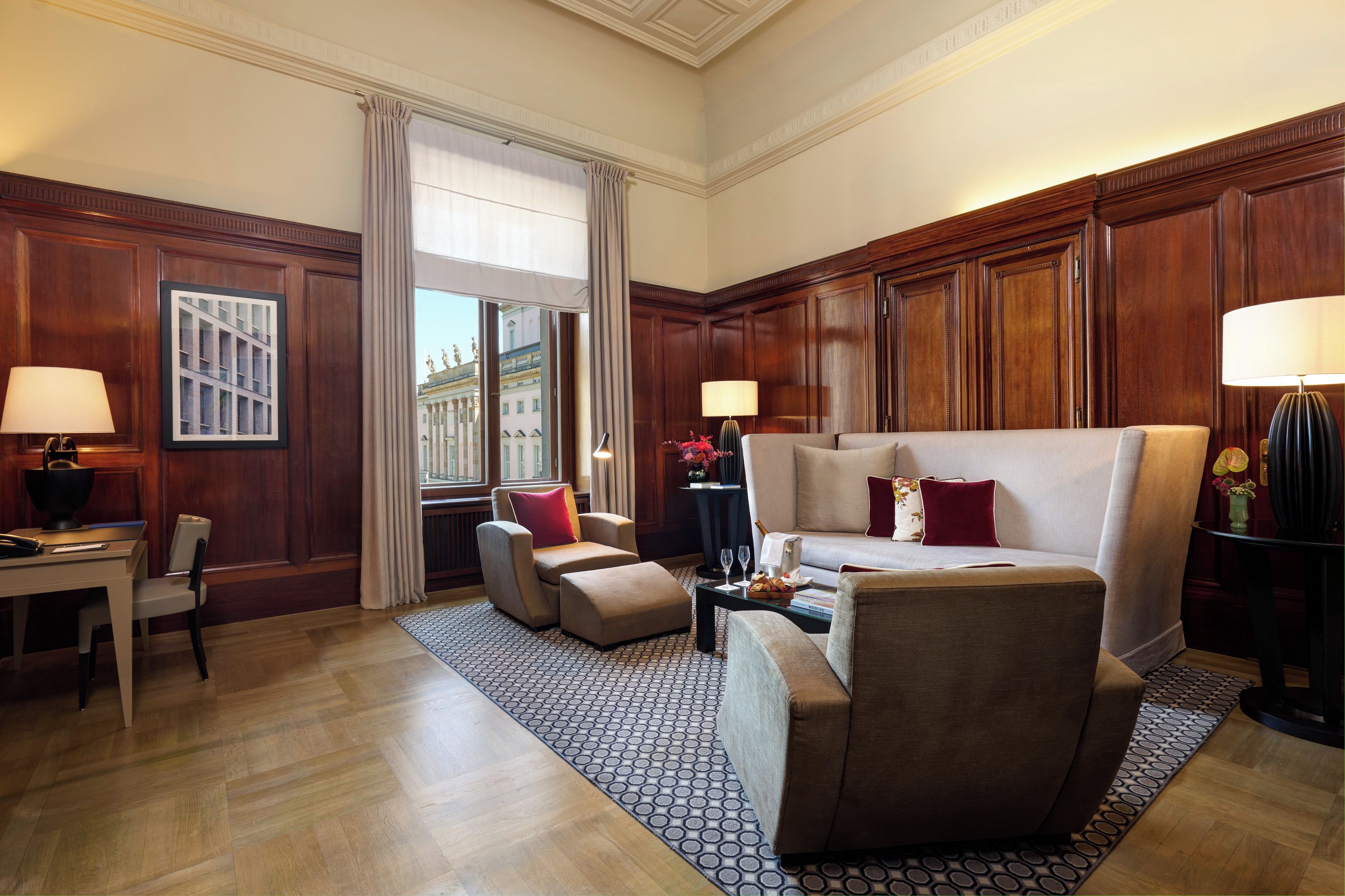 Habitación de hotel con un ventanal grande, un sofá, una silla, un escritorio y una lámpara.