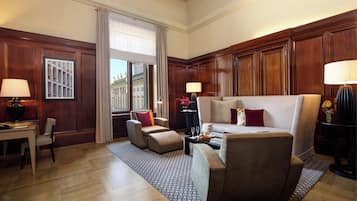 Habitación de hotel con un ventanal grande, un sofá, una silla, un escritorio y una lámpara.