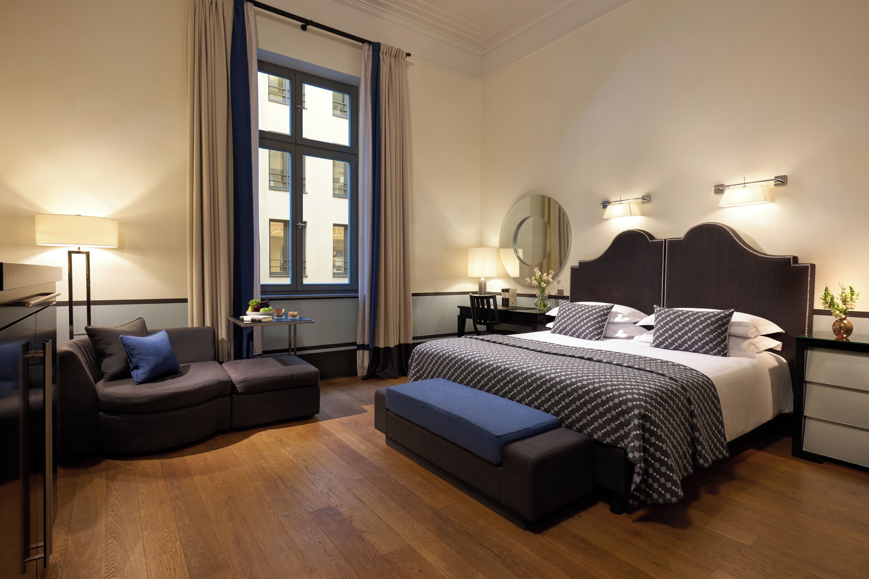 A modern hotel room with a large bed, a sofa, a desk, and a window with curtains.