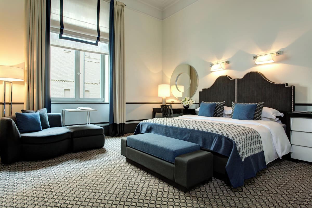 A hotel room with a large bed, a sofa, a desk, and a window with curtains.