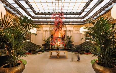 A spacious lobby with a central table, potted plants, and a high ceiling with a skylight.