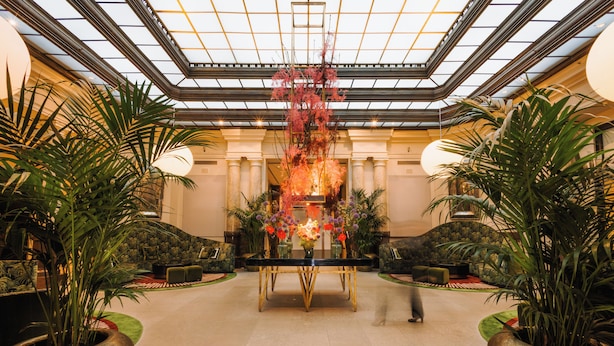 A spacious lobby with a central table, potted plants, and a high ceiling with a skylight. - Hotel De Rome Berlin (Berlin)