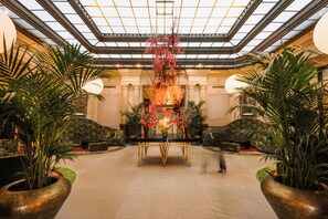A spacious lobby with a central table, potted plants, and a high ceiling with a skylight. - Hotel De Rome Berlin (Berlin)