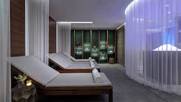 Un espacio de spa con dos camillas de masaje, una pared con panel verde y una cortina.