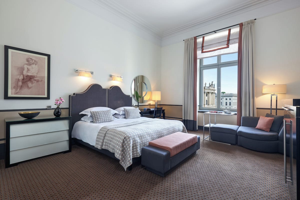 A hotel room with a large bed, a sofa, a desk, and a view of a building through the window.