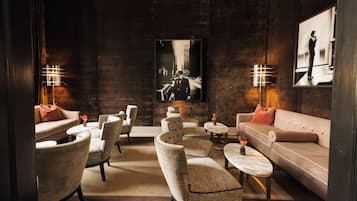 A modern lounge area with a sofa, chairs, and tables, featuring artwork and ambient lighting.