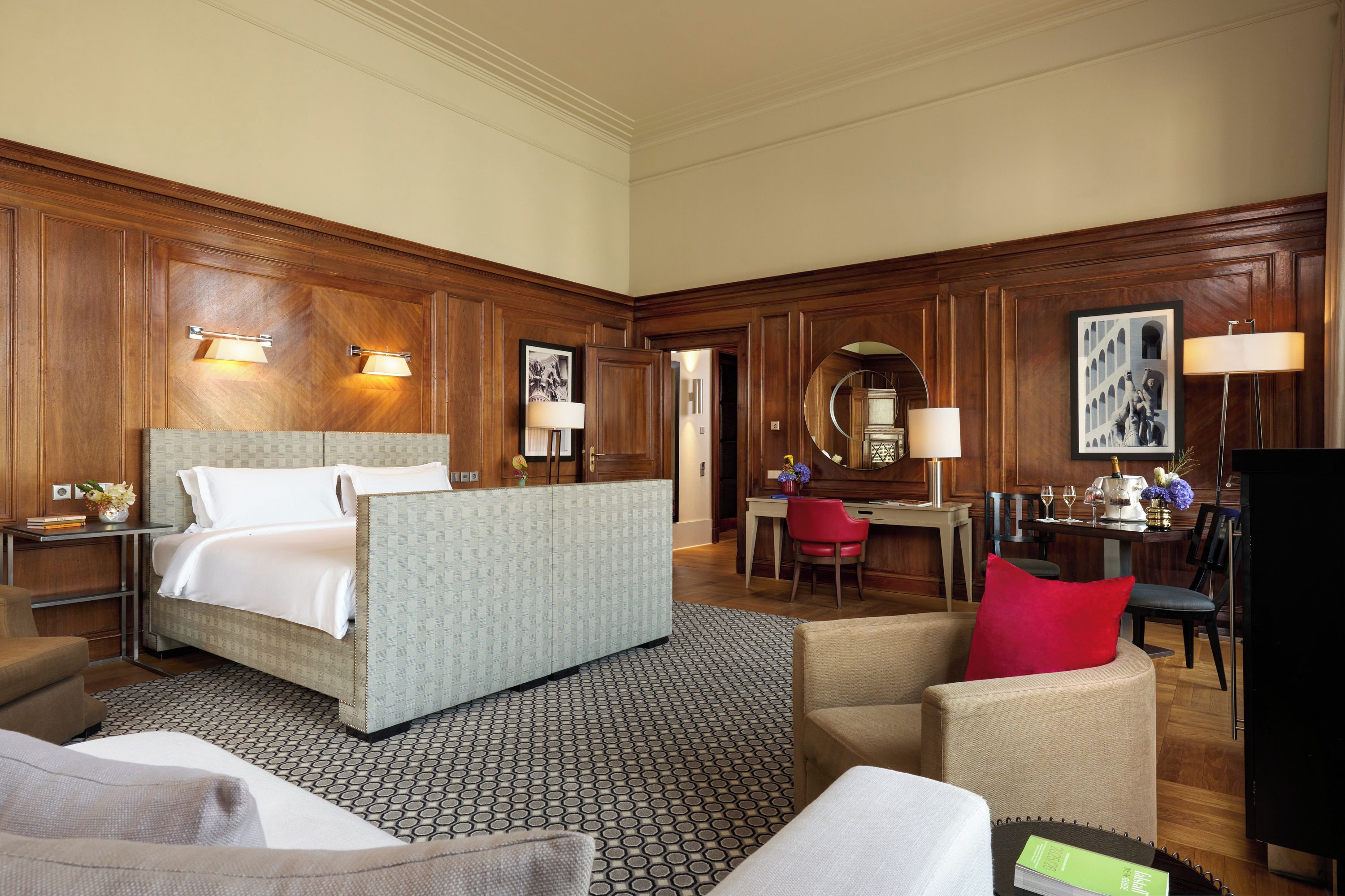 A hotel room with a bed, a desk, a chair, and a dining area.