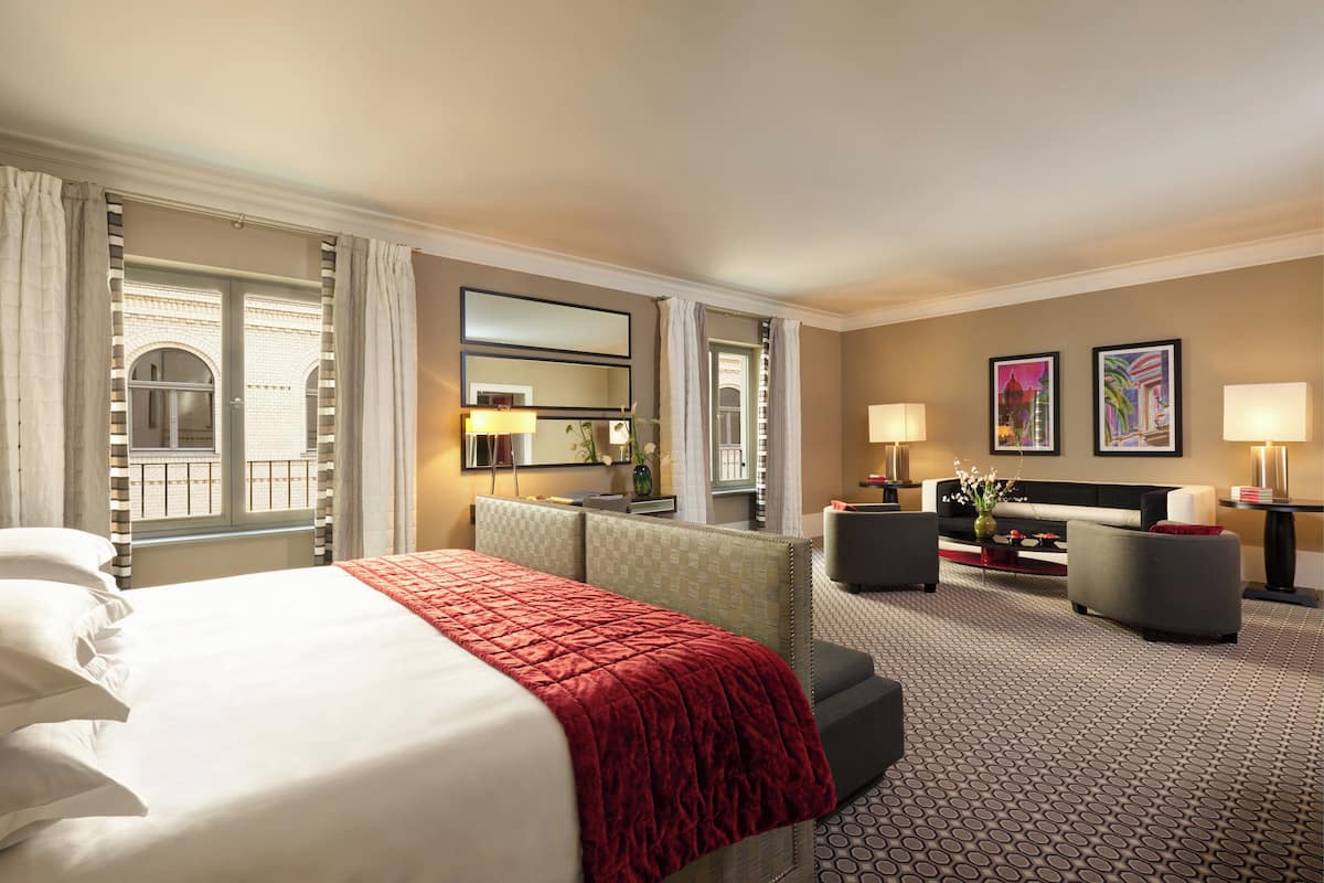 A hotel room with a large bed, a sofa, a desk, and a view of the outside.