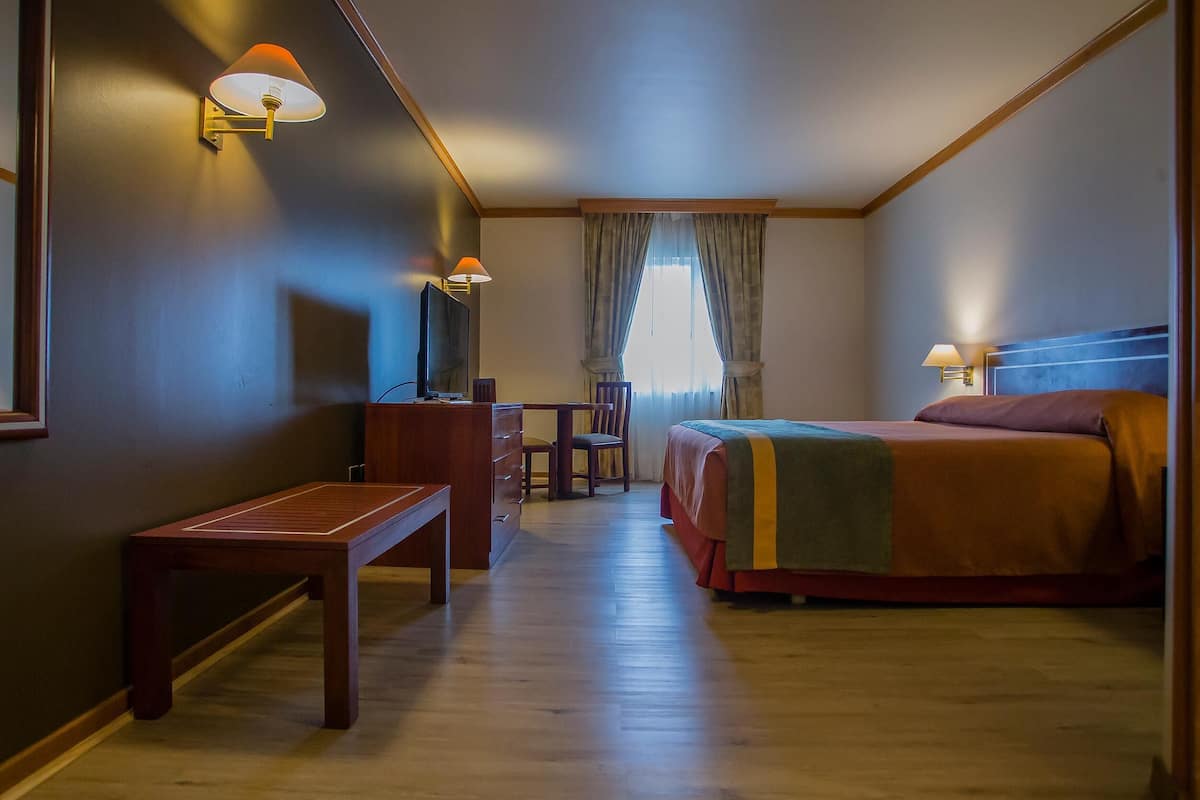 A hotel room with a bed, a desk, a chair, a television, and two wall-mounted lamps.