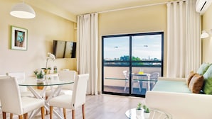 Uma sala de estar moderna com uma mesa de jantar de vidro, cadeiras brancas, um sofá e uma varanda com vista.
