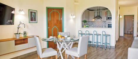 Zona pranzo con tavolo in vetro, sedie bianche e una cucina sullo sfondo.