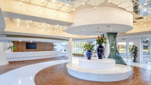 Um hall espaçoso com uma área de estar circular central, um balcão de recepção e uma grande janela com vista para o exterior.