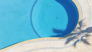 Vista aérea de uma piscina com deck ladrilhado, espreguiçadeiras e guarda-sóis.