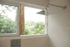 A bathroom with a shower, a window, and a view of greenery outside.