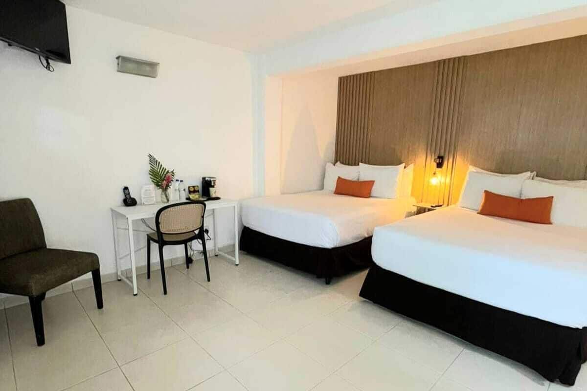 A hotel room with two beds, a desk, a chair, and a television.