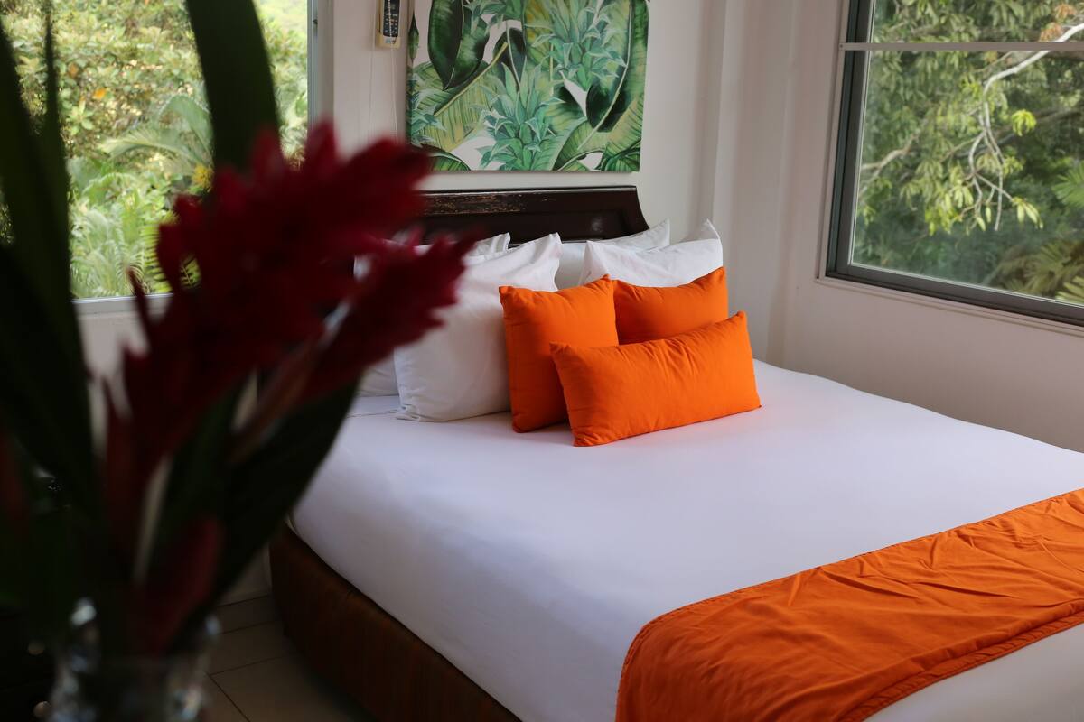 A bedroom with a bed, white bedding, and orange pillows.