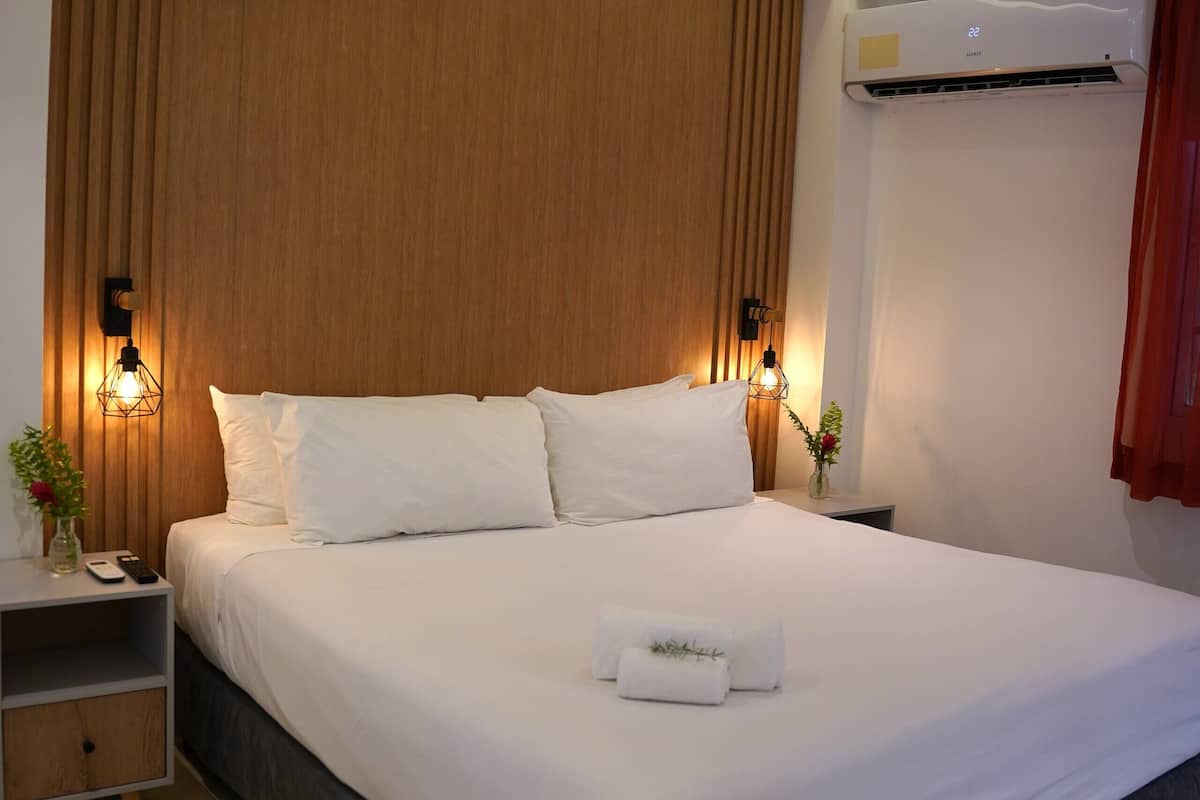 A modern hotel room with a large bed, wooden headboard, bedside lamps, and a small table with a vase and plant.