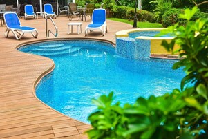 Una piscina al aire libre, sombrillas, sillones reclinables de piscina