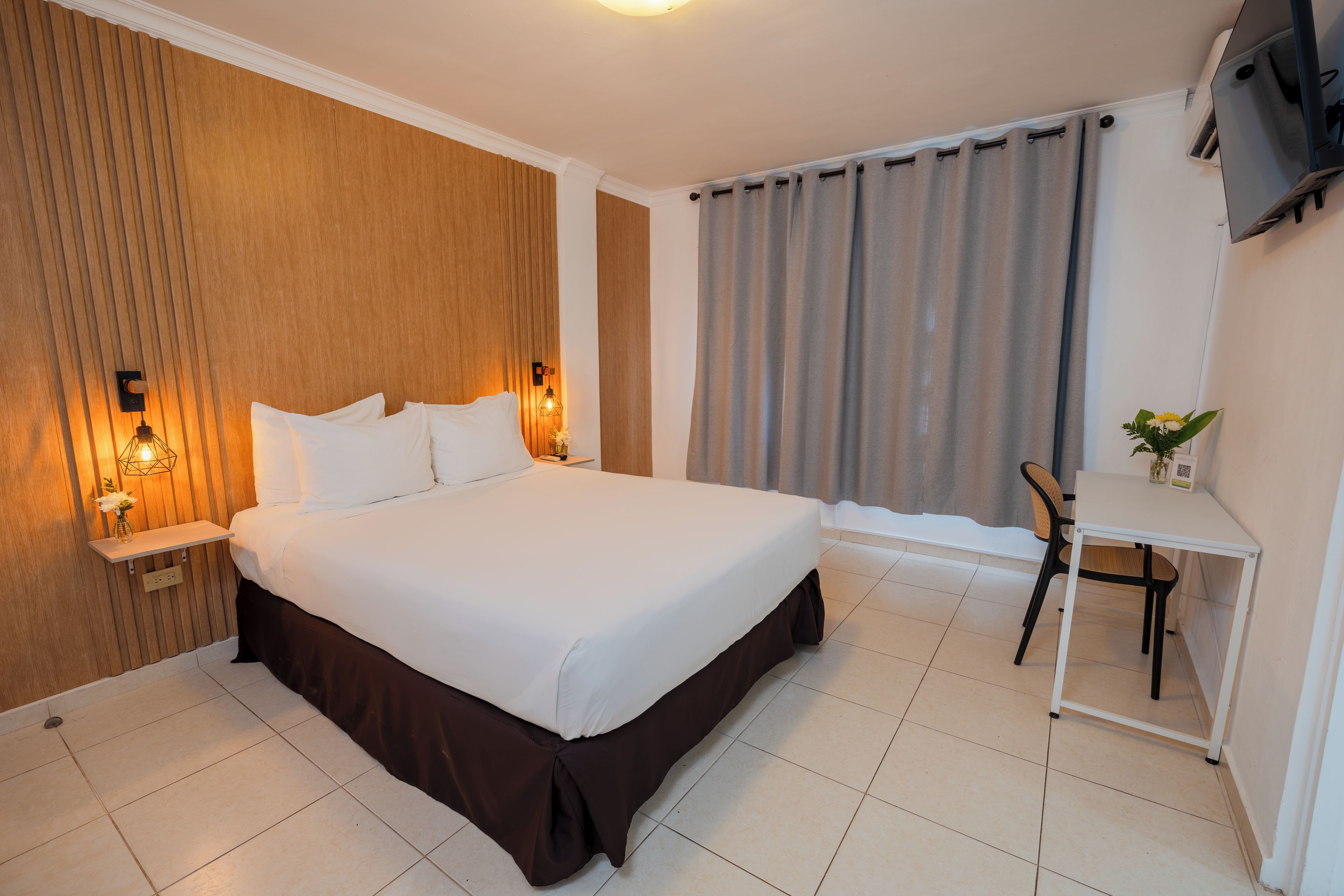 Ein Hotelzimmer mit einem großen Bett, Nachttischen, einem Schreibtisch und einem Fenster mit Vorhängen.
