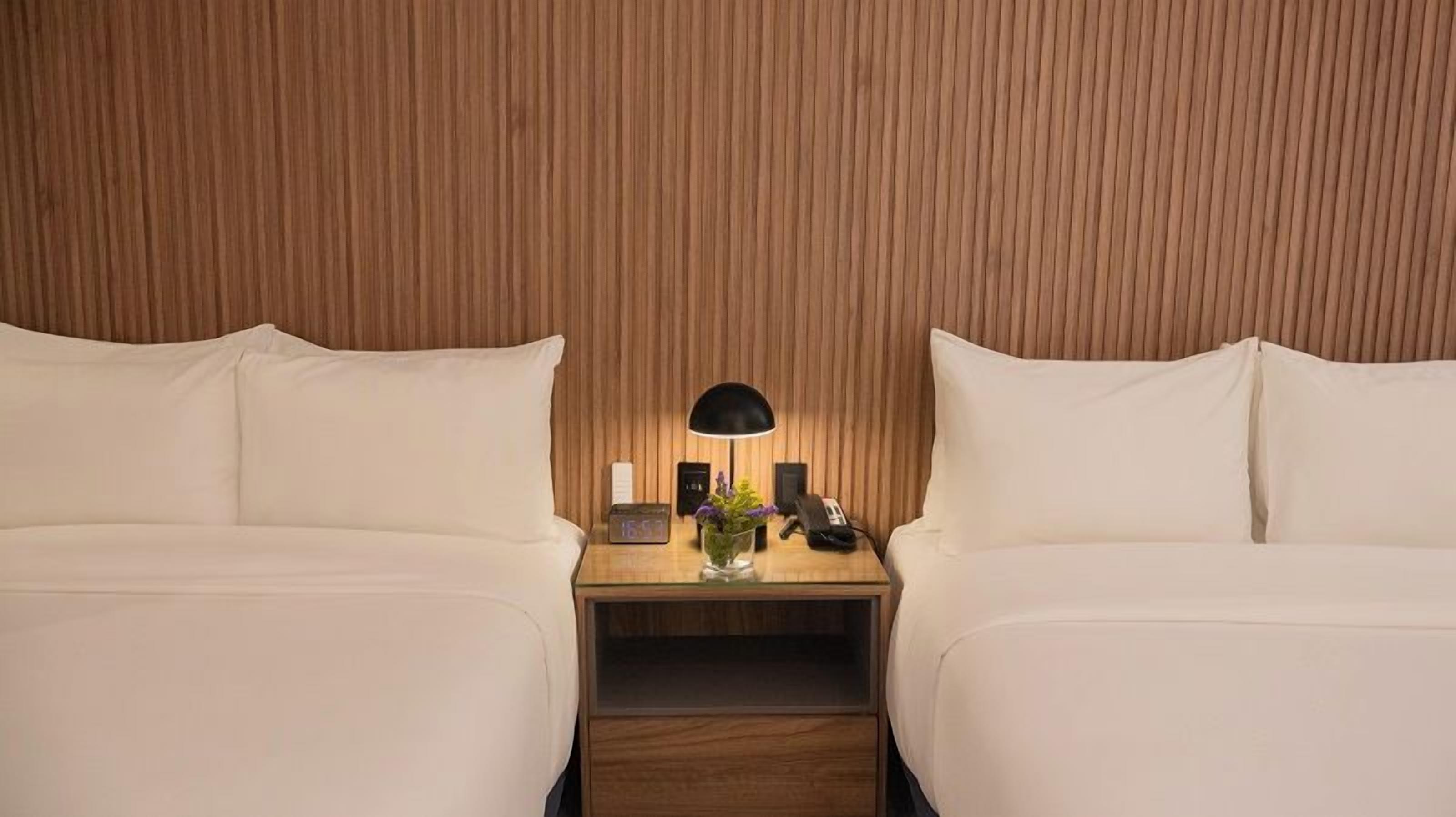 A hotel room with two beds, a nightstand with a lamp, and a wooden panel wall.