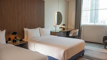A hotel room with two beds, a desk with a chair, a large mirror, and a view of the city.
