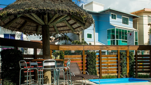A pool area with lounge chairs, a barbecue setup, and a thatched umbrella. - Pousada Mar do Leste (Florianópolis)