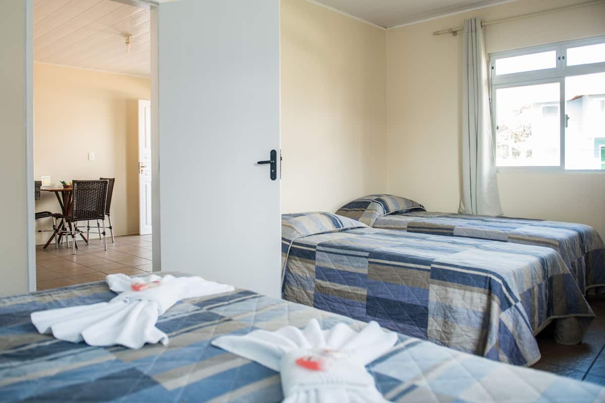Habitación de hotel con dos camas, una zona de comedor con mesa y sillas, y un ventanal con cortinas.