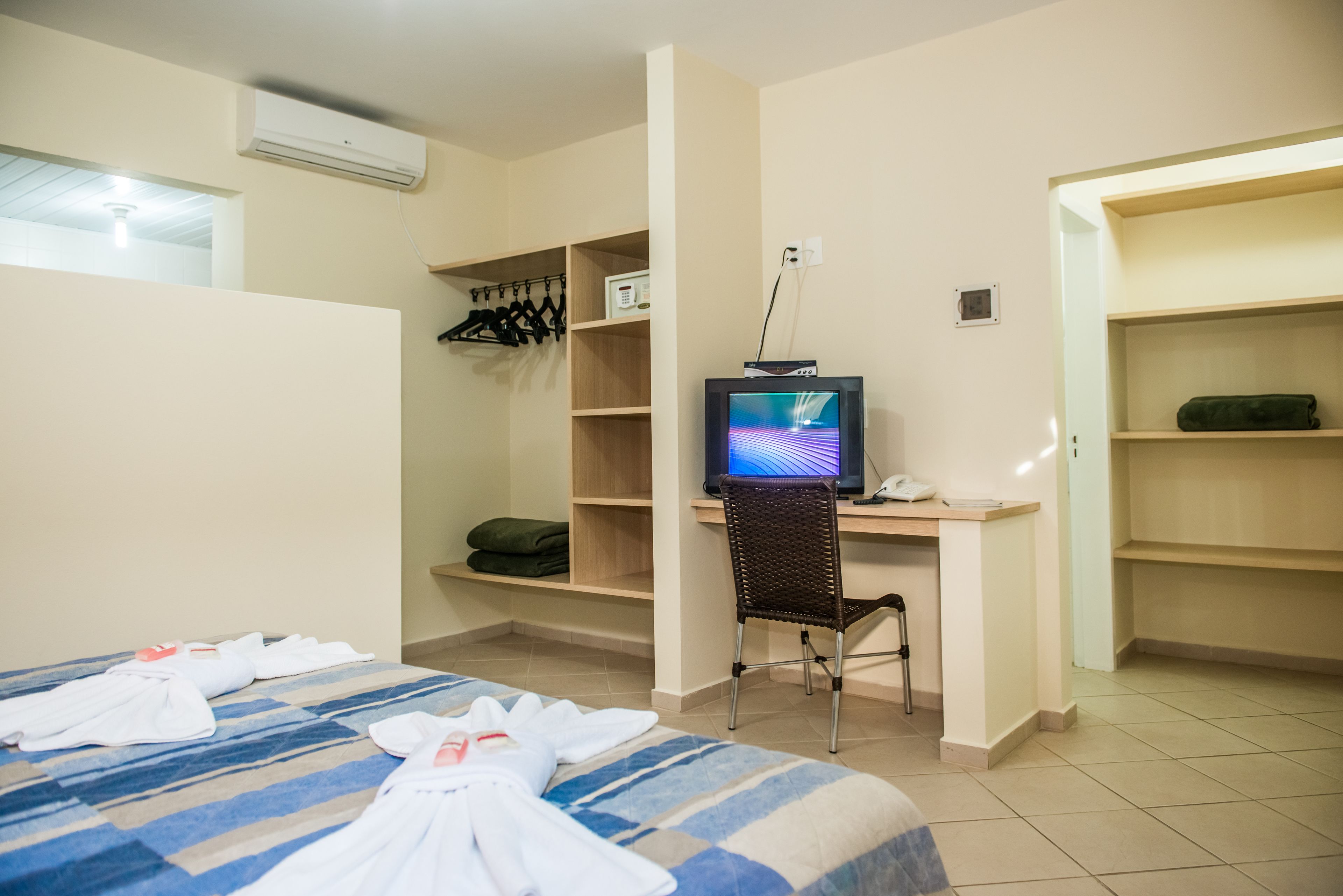 A hotel room with a bed, a desk with a computer, a chair, and a TV.