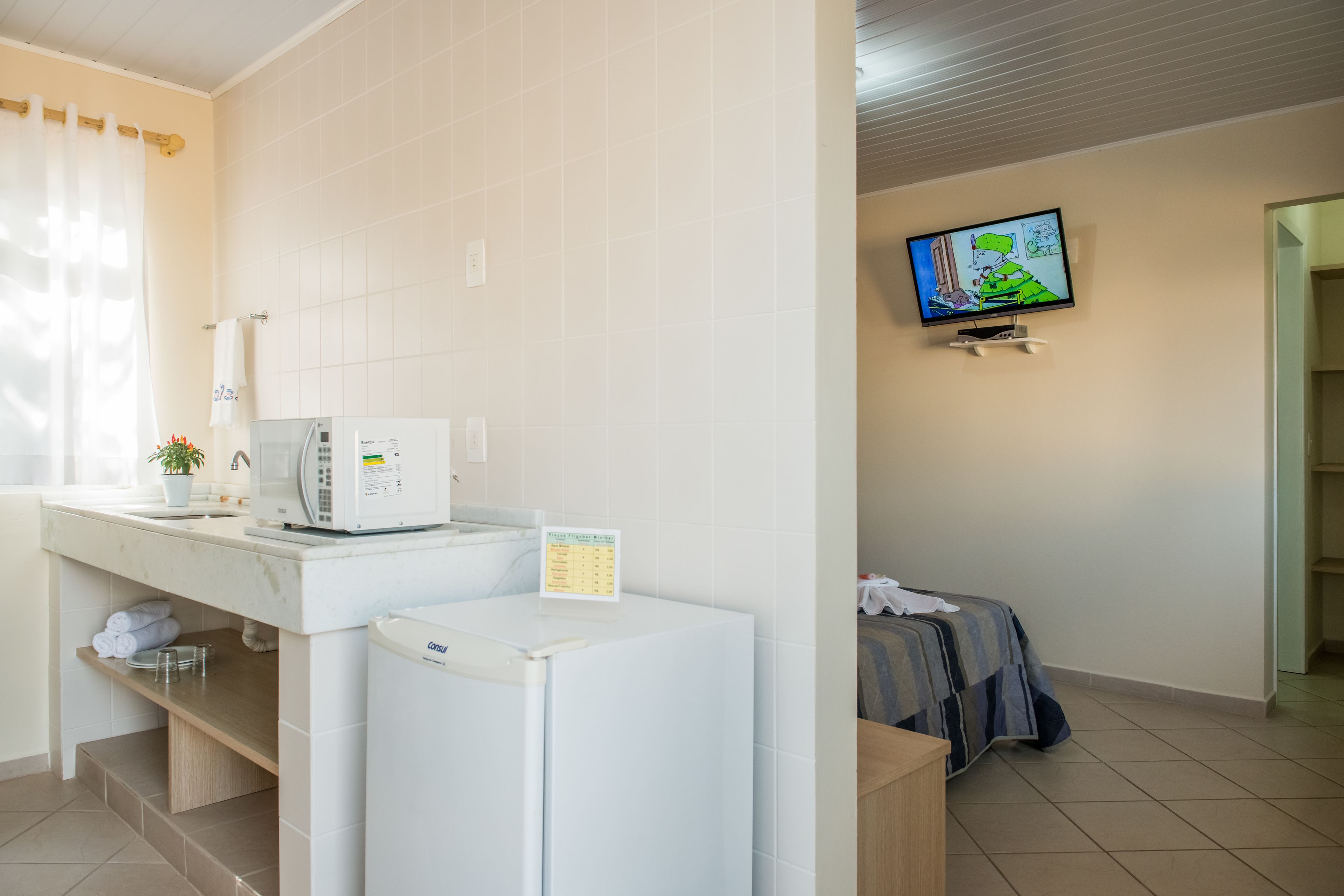 Une chambre d’hôtel équipée d’une kitchenette, d’un four à micro-ondes, d’un réfrigérateur, d’un téléviseur fixé au mur et d’un lit avec une couverture.
