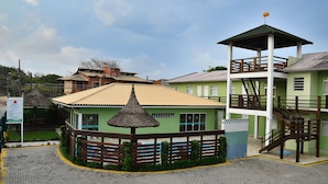 A hotel with a green building, a thatched-roof structure, and a covered area with stairs. - Pousada Mar do Leste (Florianópolis)