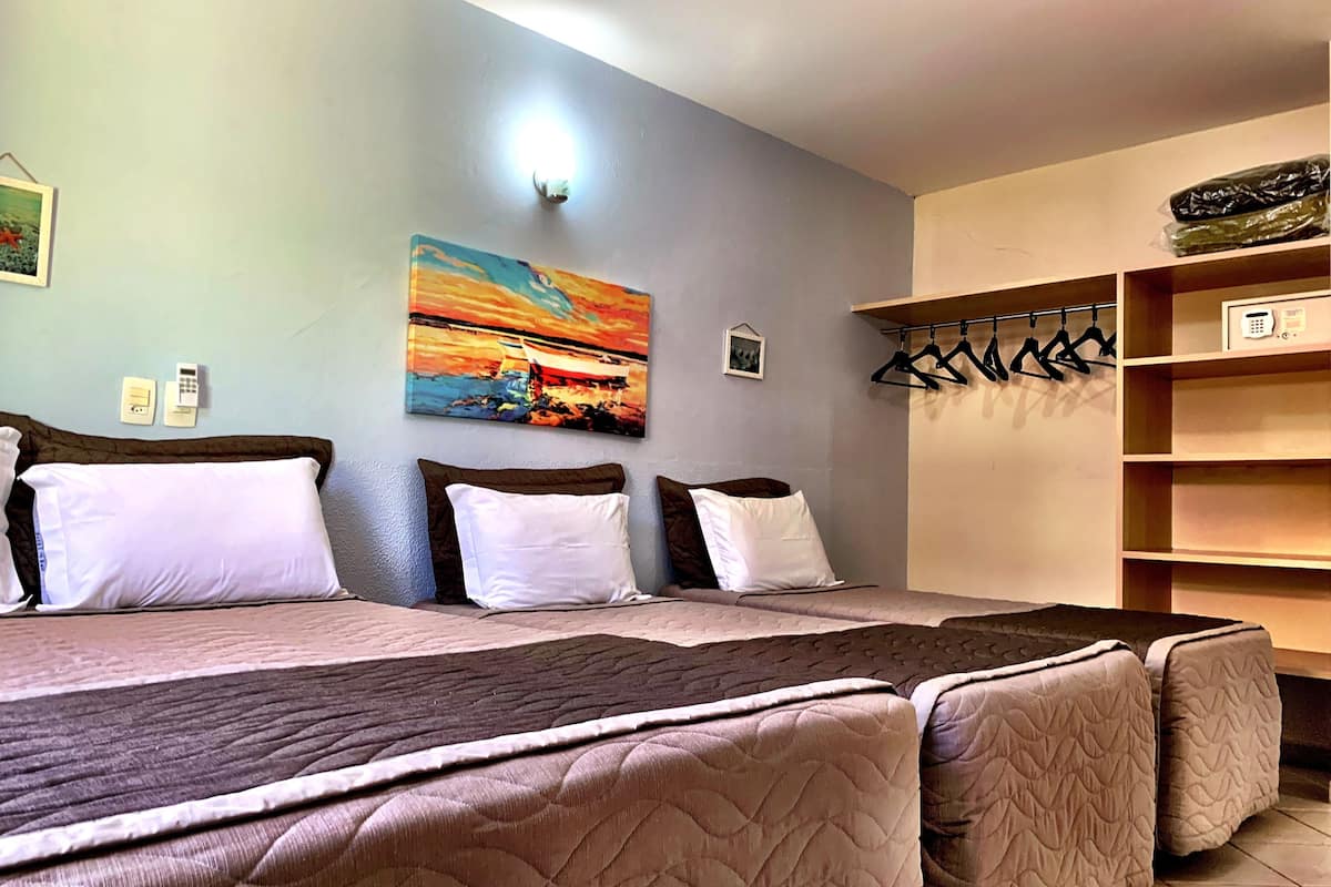 Una habitación de hotel con cama, un cuadro, perchero y estante con objetos.