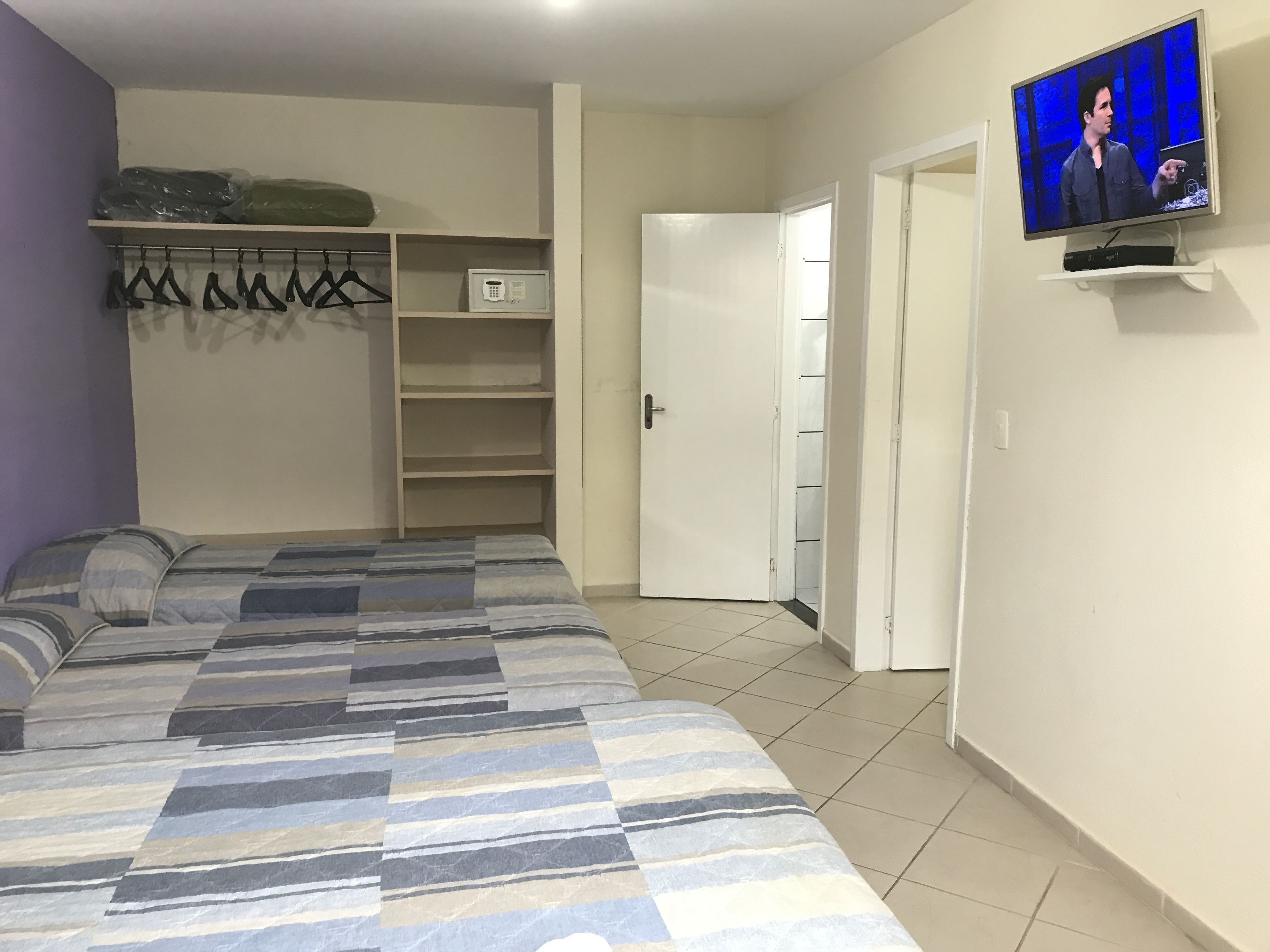 A bedroom with a bed, a TV, a wardrobe, and a door leading to another room.