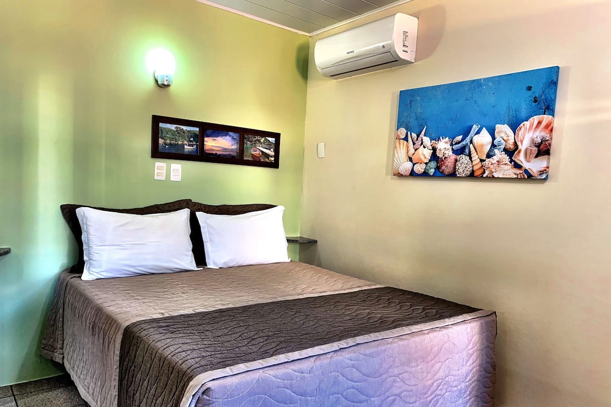 Habitación de hotel con una cama, aire acondicionado de pared, un cuadro de un puente y un cuadro concaracoles.