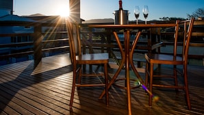 A wooden deck with a table and chairs, a bottle of wine, and two wine glasses. - Pousada Mar do Leste (Florianópolis)