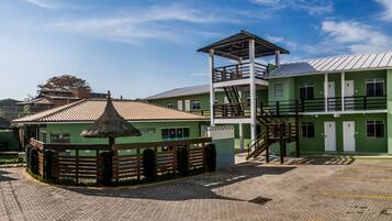A green building with a thatched-roof structure, a staircase, and a fenced area.