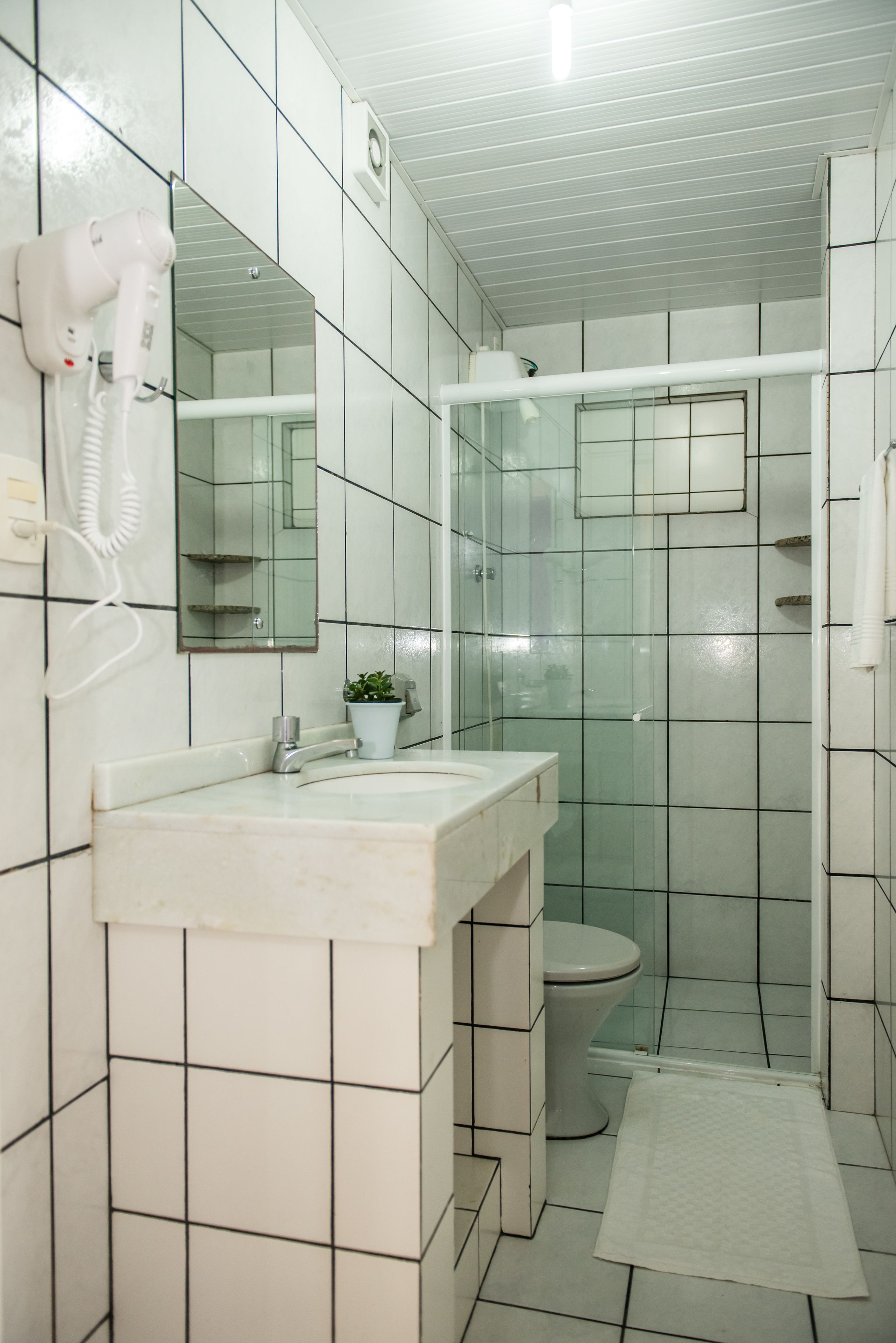 Un baño con lavamanos blanco, espejo y secador de pelo en la pared.