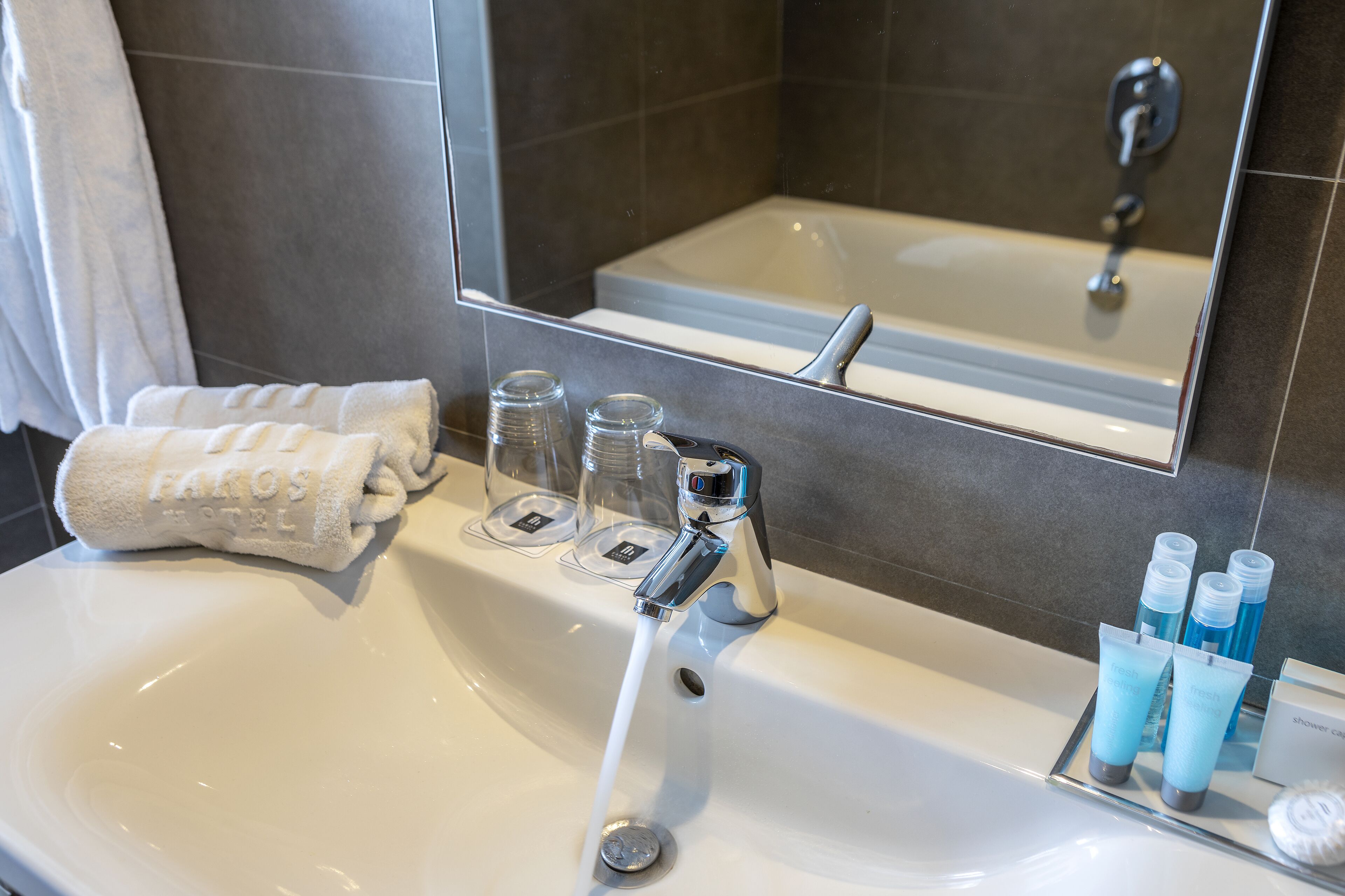 Et badeværelse med en hvid vask, et spejl, et håndklæde og toiletartikler.