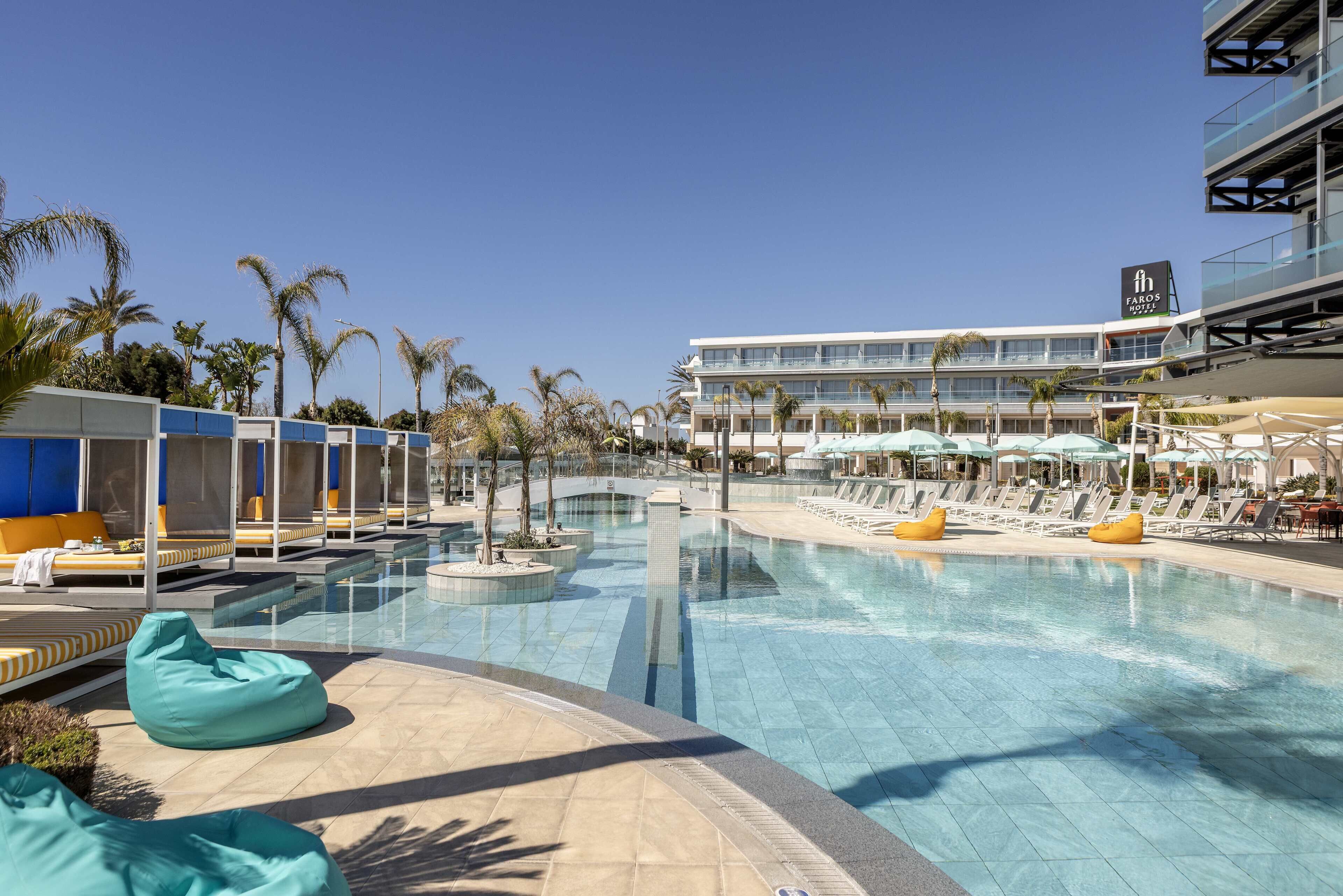 Un área de piscina con sillones de descanso, una fuente de agua y un edificio con un cartel.