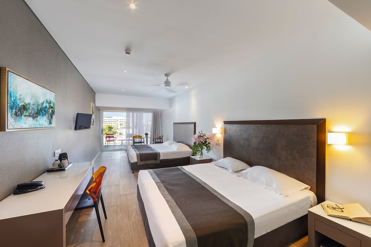 Habitación de hotel con dos camas, un escritorio y una silla. Hay un televisor en la pared y una ventana con vistas al exterior.