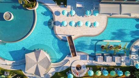 Una piscina amplia y despejada con numerosas tumbonas y sombrillas, rodeada por una zona ajardinada con palmeras y un área de estar circular.