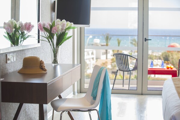 Habitación de hotel con un ventanal grande, un escritorio con un sombrero, una silla con una toalla y una cama.